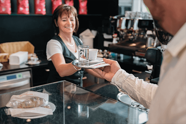 Mitarbeiterin auf Tankstelle gibt einem Kunden Kaffee